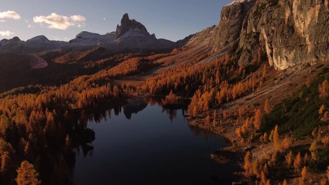 Aerial view of Lago Federa surrounded by golden larch trees and dramatic mountain peaks reflecting in the calm water in Cortina d'Ampezzo, Veneto, Italy.