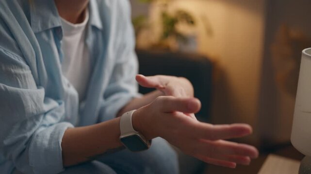Close-up of adult woman's hands gently rubbing together while relaxing on a sofa at home, representing self-soothing, stress relief, comfort, emotional wellbeing and personal care.