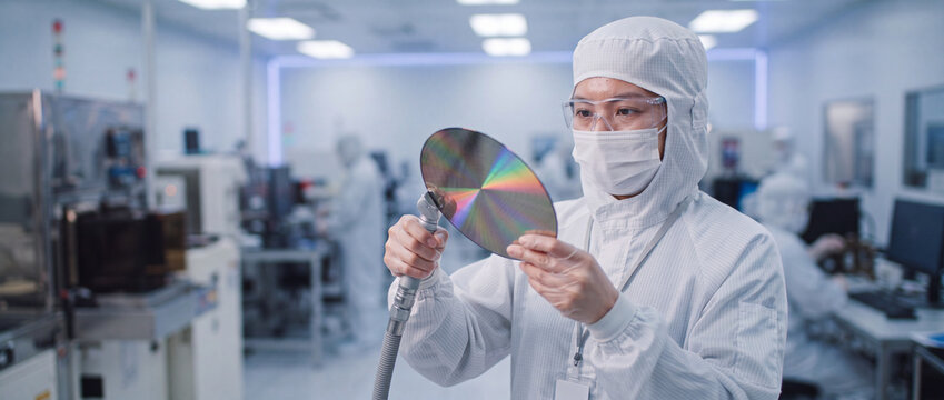 Silicon wafer inspection in cleanroom laboratory by an engineer in protective sterile suit checking microchip rainbow surface for semiconductor manufacturing quality control