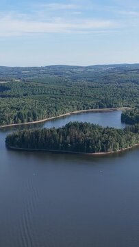 A forested island surrounded by calm water in Lac des Settons, located in the Morvan region of France, aerial vertical 9:16 view.
