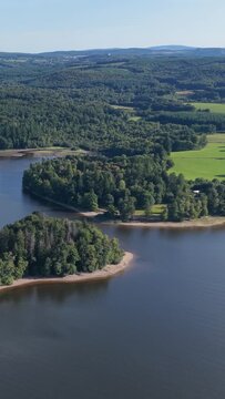 A lush, forested island and surrounding shoreline on Lac des Settons in Morvan, France, aerial vertical 9:16 view.