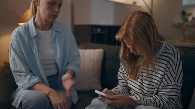 Close-up of teenage girl scrolling social media on smartphone while concerned mother tries to talk, illustrating excessive screen time, digital distraction and family communication problems.
