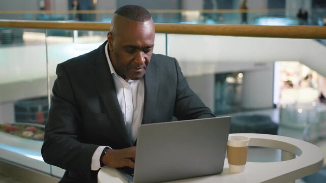Puzzled African American middle-aged business man thinking working with computer finding answer come up with idea typing computer mature businessman male agent professional think work online in cafe