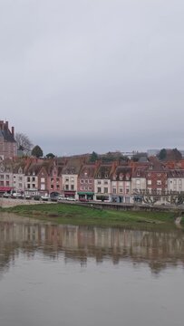 The charming riverfront of Gien city center in France. The clip captures a row of colorful historic townhouses with traditional roofs, reflected in the calm river below, vertical 9:16 view.
