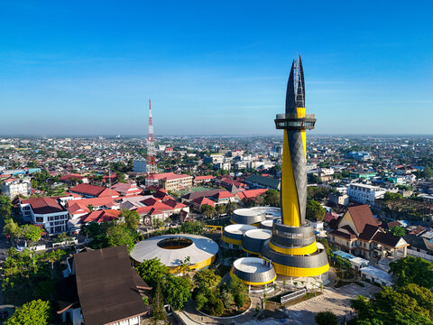 Aerial view of the Monument of Pal 0 Banua with its yellow and black design, surrounded by urban rooftops and trees in Kecamatan Banjarmasin Tengah, Kalimantan Selatan, Indonesia.