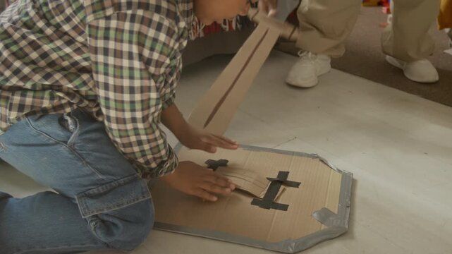 African American teenager and kid playing with homemade cardboard swords and shields in bedroom. Video is perfect for parenting campaigns and creative education advertisements