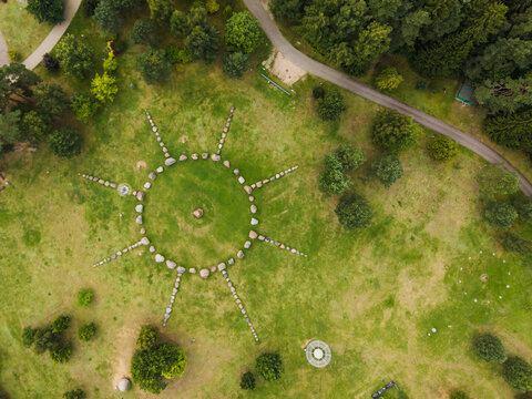 Aerial view of the sun-shaped stone formation at the Lithuanian Museum of Ethnocosmology, surrounded by green grass and trees in Kulionys, Utenos apskritis, Lithuania.