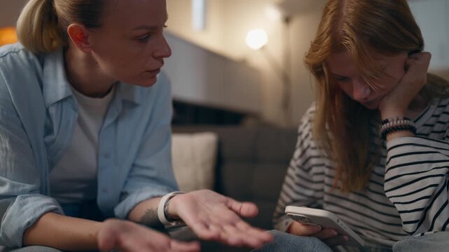 Mother trying to talk to teenage daughter while girl remains focused on smartphone, illustrating teenage rebellion, difficult adolescence, communication problems and generation gap.