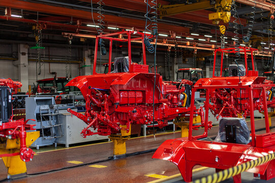Industrial assembly line of red agricultural tractors at manufacturing plant. Heavy industrial manufacturing, process of assembling agricultural machinery, automation, modern agriculture.