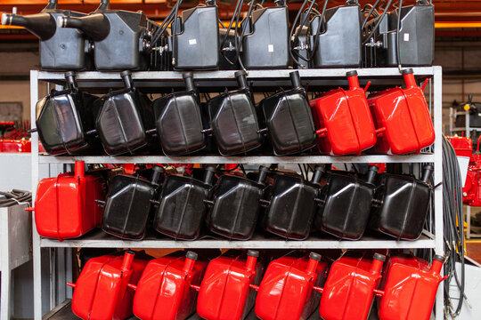 Rows of new red and black fuel tanks stored on metal shelving in heavy manufacturing plant.Industrial manufacturing, supply chain, spare parts, and agricultural machinery production.