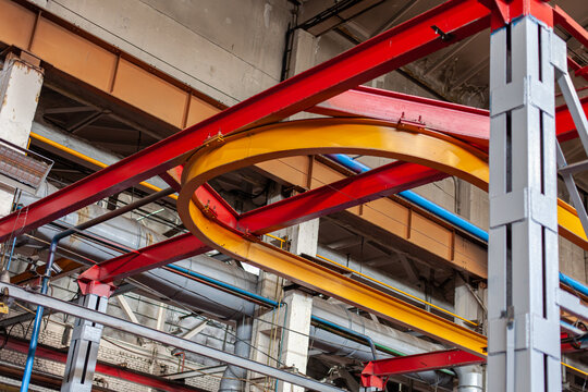 Low angle view of industrial factory ceiling with red and yellow overhead crane tracks. Industrial architecture, engineering infrastructure, heavy manufacturing environment.