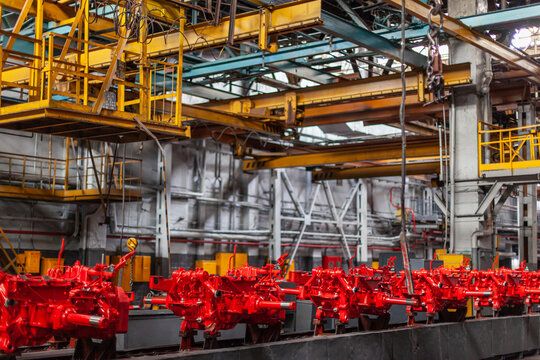 Assembly line of red tractor chassis components in heavy machinery factory.Mechanical engineering, large-scale production, industrial technology, heavy manufacturing.