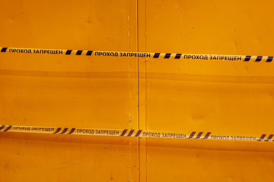 Close-up shot of bright yellow metal door surface secured with caution tape "NO ENTRY". Safety, restriction, prohibition, industrial security, restricted access.
