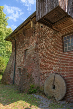 Historic red brick mill building facade with large round stone millstone leaning against wall
