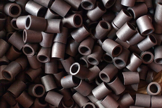 Pile of small industrial metal bushings or sleeves in tractor factory workshop. Raw materials and components used in assembly of heavy machinery. Industrial efficiency, metalwork, mechanical parts.