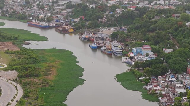 Overhead drone shot of a river shipyard, aquatic vegetation, and surrounding urban settlements