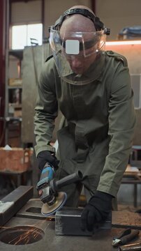 Vertical video of young adult Caucasian welder wearing protective face shield and grinding metal piece with angle grinder. Footage is perfect for industrial safety and manufacturing ads