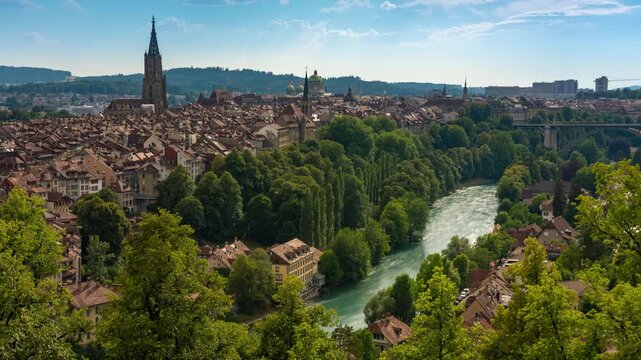 Time lapse of Bern old town skyline with rushing clouds over Aare river, medieval architecture, gothic cathedral spire, and historic bridges in Switzerland