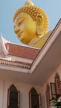 Close up view of golden Buddha statue with ornate temple roof detail against blue sky at Wat Paknam Phasi Charoenin Bangkok city, Thailand. Portrait of Big Seated Buddha. Travel and tourism in Asia