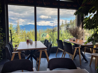 Fototapeta premium Cozy restaurant interior with large windows overlooking a scenic mountain landscape and pine forest, perfect for a tranquil getaway.