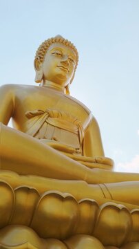 Giant golden buddha statue sitting on lotus base against blue sky with clouds at Wat Paknam Phasi Charoen in Bangkok city, Thailand. Low angle view of Big Seated Buddha. Travel and tourism in Asia