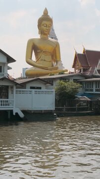 Big Seated Buddha Statue at Wat Paknam Phasi Charoen temple on the river bank in Bangkok city, Thailand. Giant golden buddha statue rising above temple rooftops. Vertical orientation