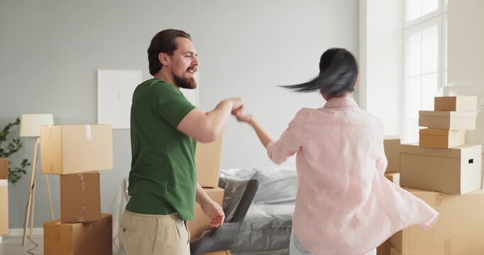 Couple dancing amid moving boxes in home. Happy man leads woman in a sunny apartment, packed cartons frame space, marking a fresh start together. Theme is joyful relocation and homeownership