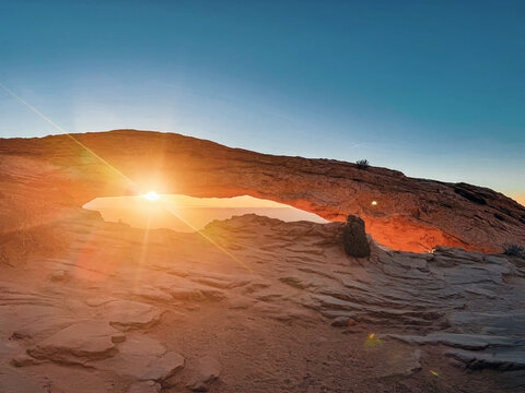 View of Mesa Arch in Canyonlands National Park at sunrise with golden light illuminating the red sandstone rock formations in Moab, Utah, United States.