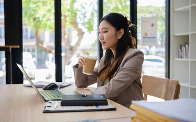 Fototapeta premium Young Asian businesswoman reviewing documents while working at her office desk.