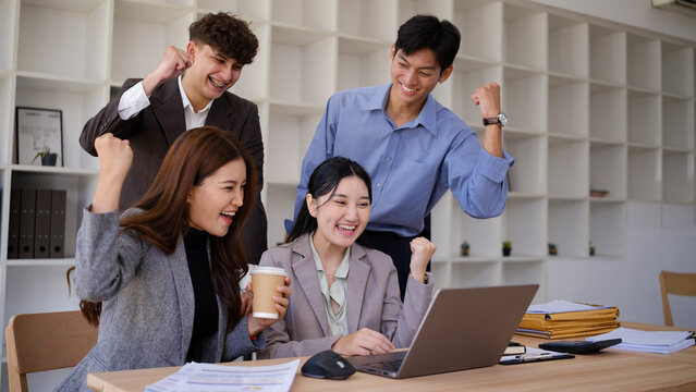 Happy diverse business team celebrating project success around a laptop.