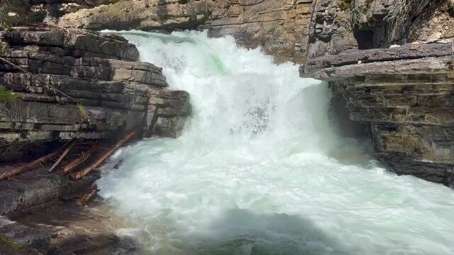 Johnston Creek river in Johnston Canyon in the Banff National Park. British Columbia, Canada. Water flows rapidly over rocks in a gorge, creating foam and splashes with greenery visible in the backgro