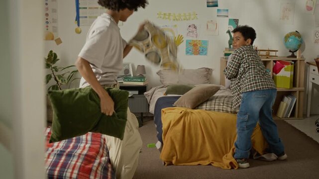 Black teenager and child having playful pillow fight in bedroom, laughing and throwing pillows. Video is perfect for family lifestyle promos and parenting campaigns