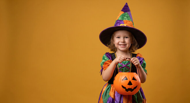 Cute little girl in witch costume holding Halloween pumpkin