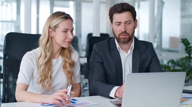 Focused business team two executives working with laptop diagrams at table Caucasian man talk with woman using modern technology businessman businesswoman with documents talking pointing at screen