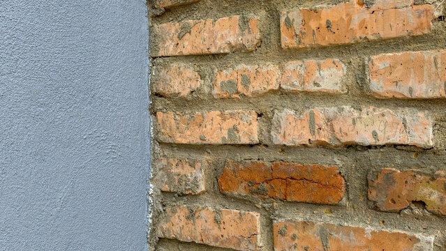 Contrasting textures presenting a rough orange brick wall with visible mortar next to a smoothly plastered grey wall, forming an architectural corner detail