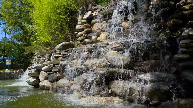 Stone waterfall flowing into small pond in city park in Istanbul. Water splashing over rocks creating fresh atmosphere