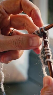 Vertical video: Knitting hands inserting needle in loop, making stitches using light yarn on porch