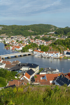 View of the town of Mandal featuring white houses with red roofs, a bridge crossing the river, and lush green hills in Mandal, Agder, Norway.