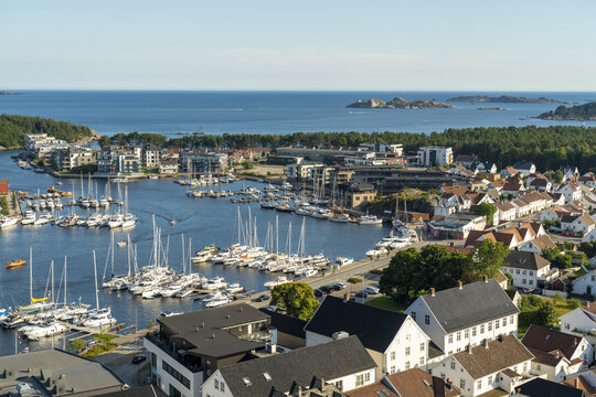 View of the harbor in Mandal filled with sailboats and yachts, surrounded by traditional white houses and lush greenery in Mandal, Agder, Norway.