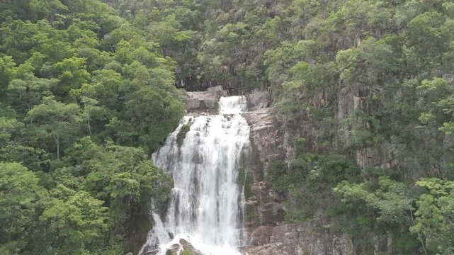 Aerial view of waterfall cascading down rocky cliffs surrounded by dense green forest in Chapada dos Veadeiros, Alto Paraiso de Goias, Goias, Brazil.