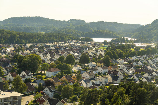 View of the town of Mandal with its characteristic white wooden houses, lush green trees, and surrounding hills in Mandal, Agder, Norway.