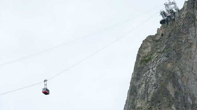 Brevent cable car red cabin ascending towards top summit station on steep rocky cliff in Chamonix Mont Blanc valley, alpine gondola ropeway transport in French Alps mountain landscape during summer