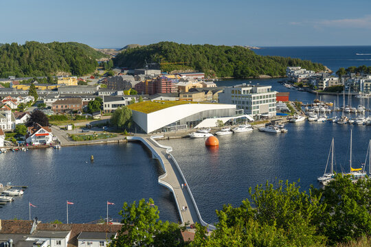 View of the modern Buen Kulturhus and the pedestrian bridge spanning the harbor with boats moored at the docks in Mandal, Agder, Norway.