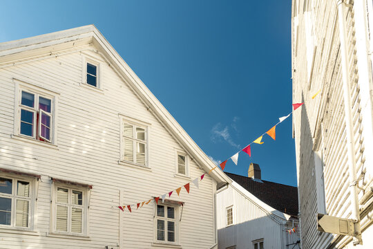 View of traditional white wooden houses adorned with colorful bunting under a clear blue sky in Mandal, Agder, Norway.