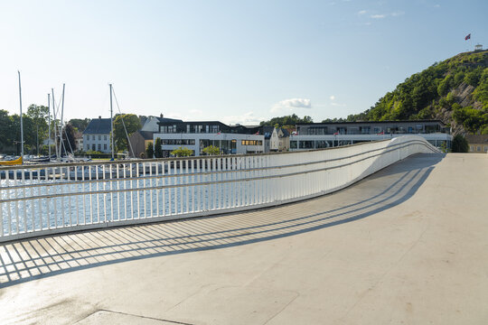 View of the modern pedestrian bridge in Mandal with a marina, sailboats, and coastal buildings in the background, Mandal, Agder, Norway.