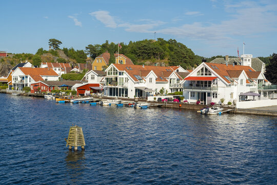 View of the coastal town of Mandal with its characteristic white wooden houses, red-tiled roofs, and small boats moored along the waterfront in Mandal, Agder, Norway.