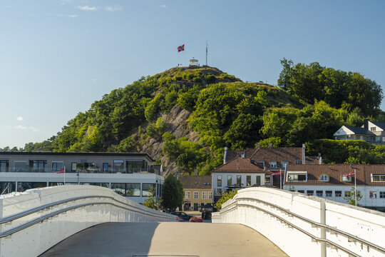 View of the white bridge leading towards the town of Mandal with the prominent Uranienborg hill and Norwegian flag in the background in Mandal, Agder, Norway.