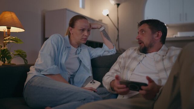 Frustrated couple experiencing a marital crisis while sitting on the couch in the living room, engaged in a heated argument and discussing serious relationship problems and family issues