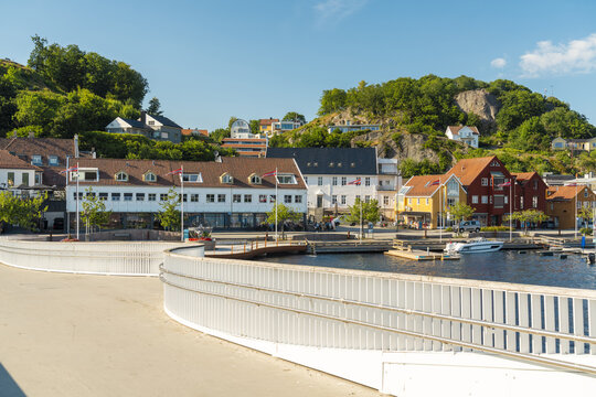 View of the harbor and colorful waterfront buildings in Mandal with a modern bridge in the foreground and a rocky hill under a clear blue sky in Mandal, Agder, Norway.