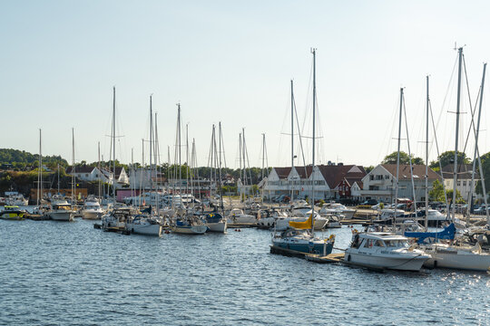 View of sailboats and motorboats docked in the harbor of Mandal with white buildings in the background under a clear sky in Mandal, Agder, Norway.